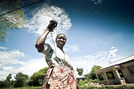 坦桑尼亚妇女举着一个现收现付的太阳能设备。Flickr / Angaza
